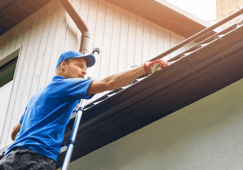 Professional technician on a ladder performing gutter system repairs and maintenance on a residential home.